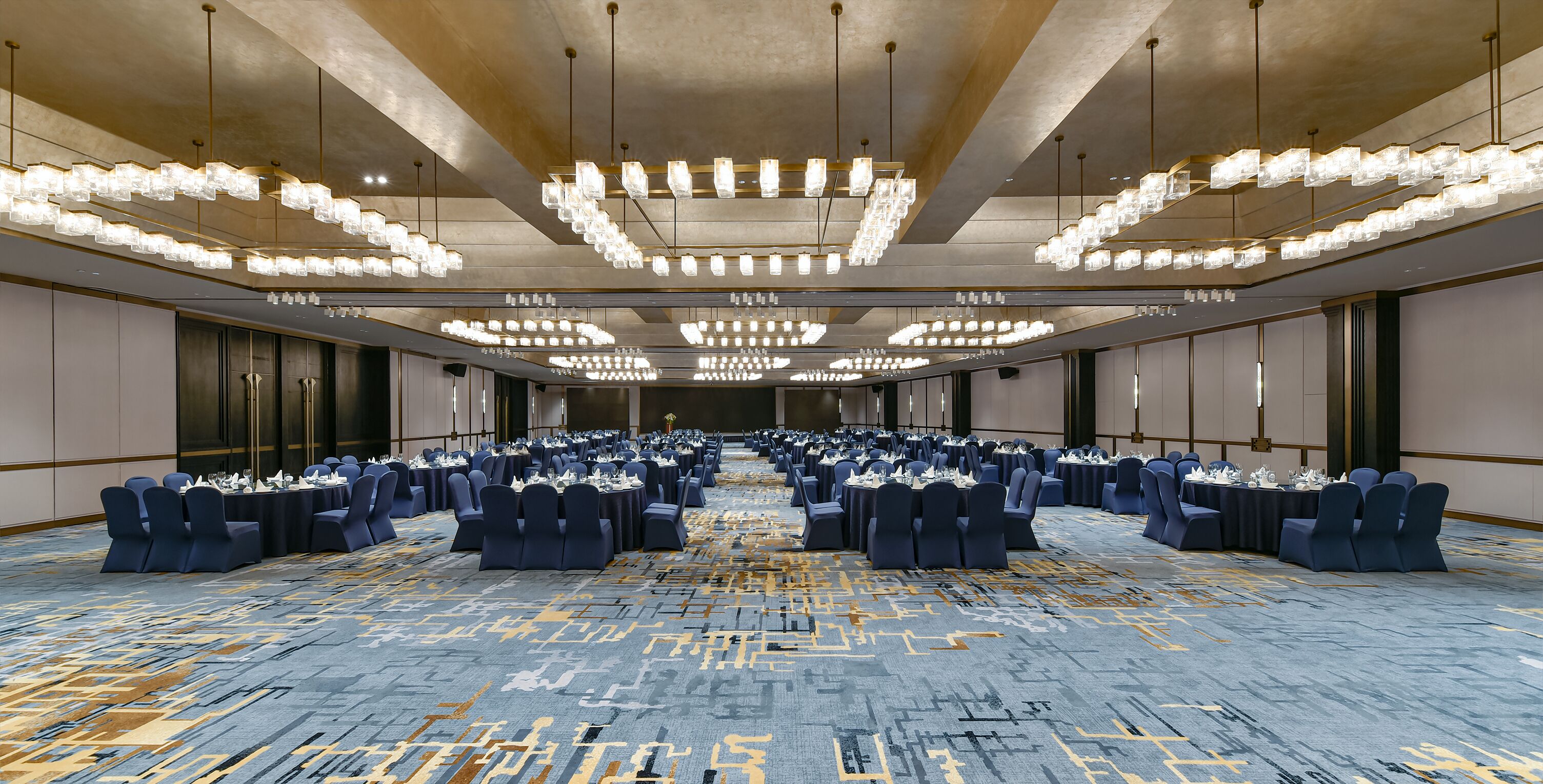 A large conference room with rows of tables and chairs, overhead lighting, and a patterned carpet.