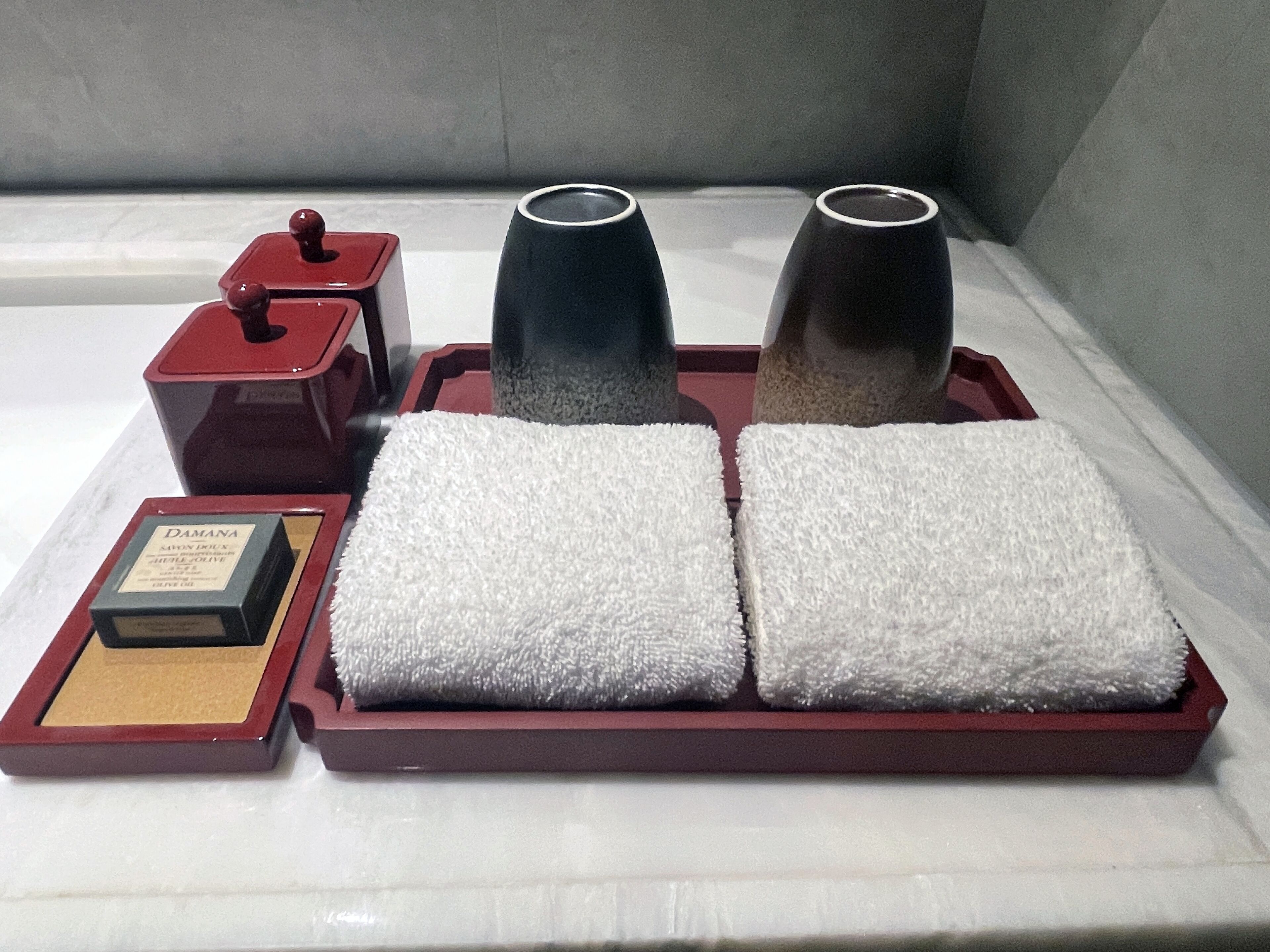 A set of toiletries on a tray, including a soap bar, two bottles, and two towels.