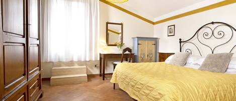 Un dormitorio con cama, un armario de madera, un escritorio con silla, un espejo y una lámpara.