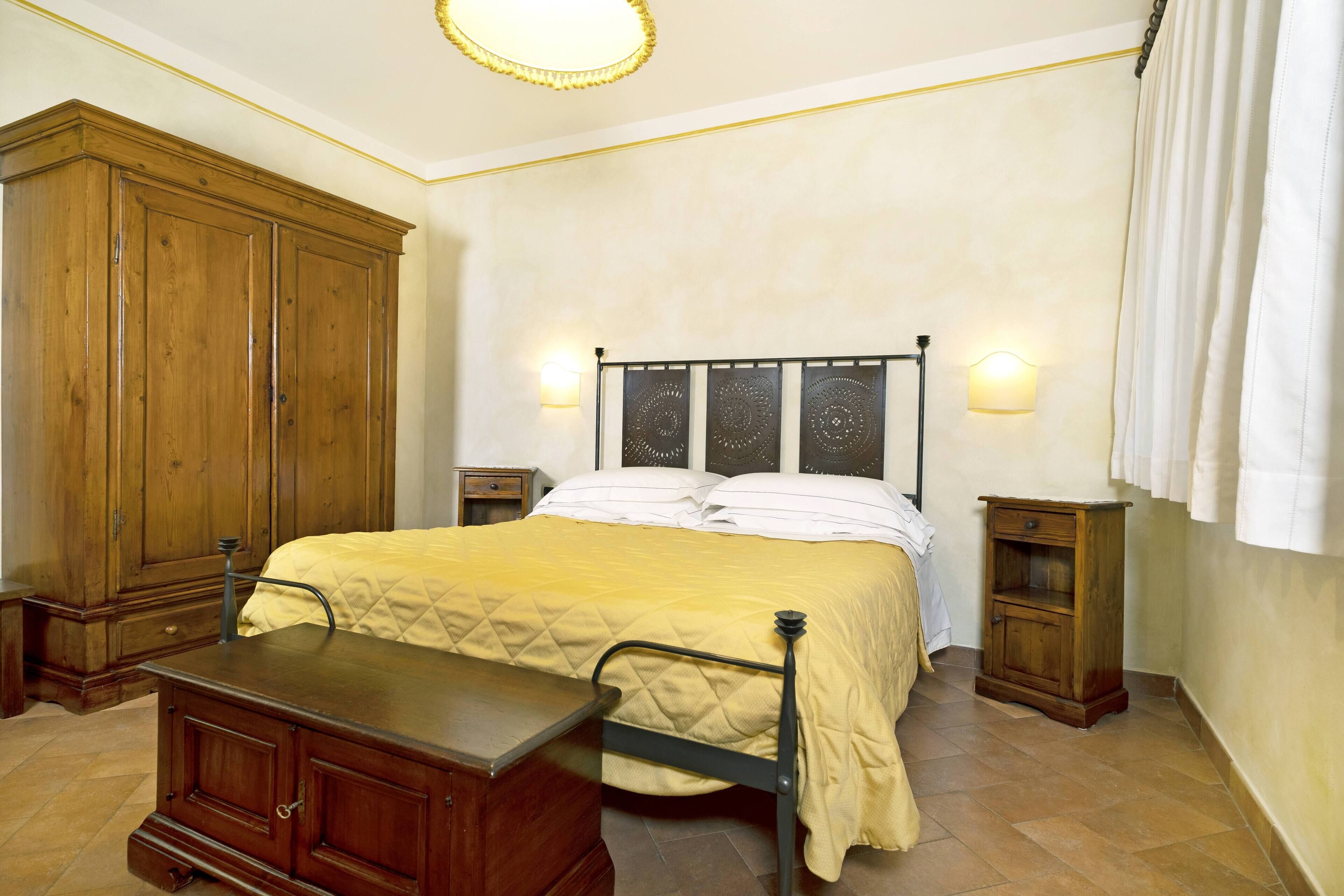 Ein Schlafzimmer mit großem Holzschrank, einem Bett mit gesteppter Bettdecke, zwei Nachttischen mit Lampen und einer kleinen Holzkommode.