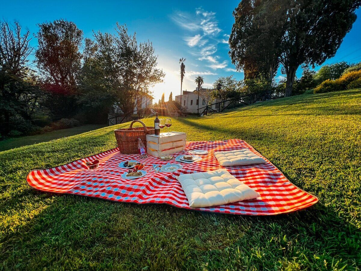 Un montaje para picnic en un campo cubierto de césped, con una manta de cuadros, comida y una cesta.