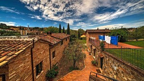 A courtyard with brick buildings, a stone wall, and a view of the surrounding town. - Borgo Grondaie (Siena)