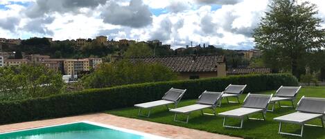 Piscina con sillones de descanso y vista a un pueblo.
