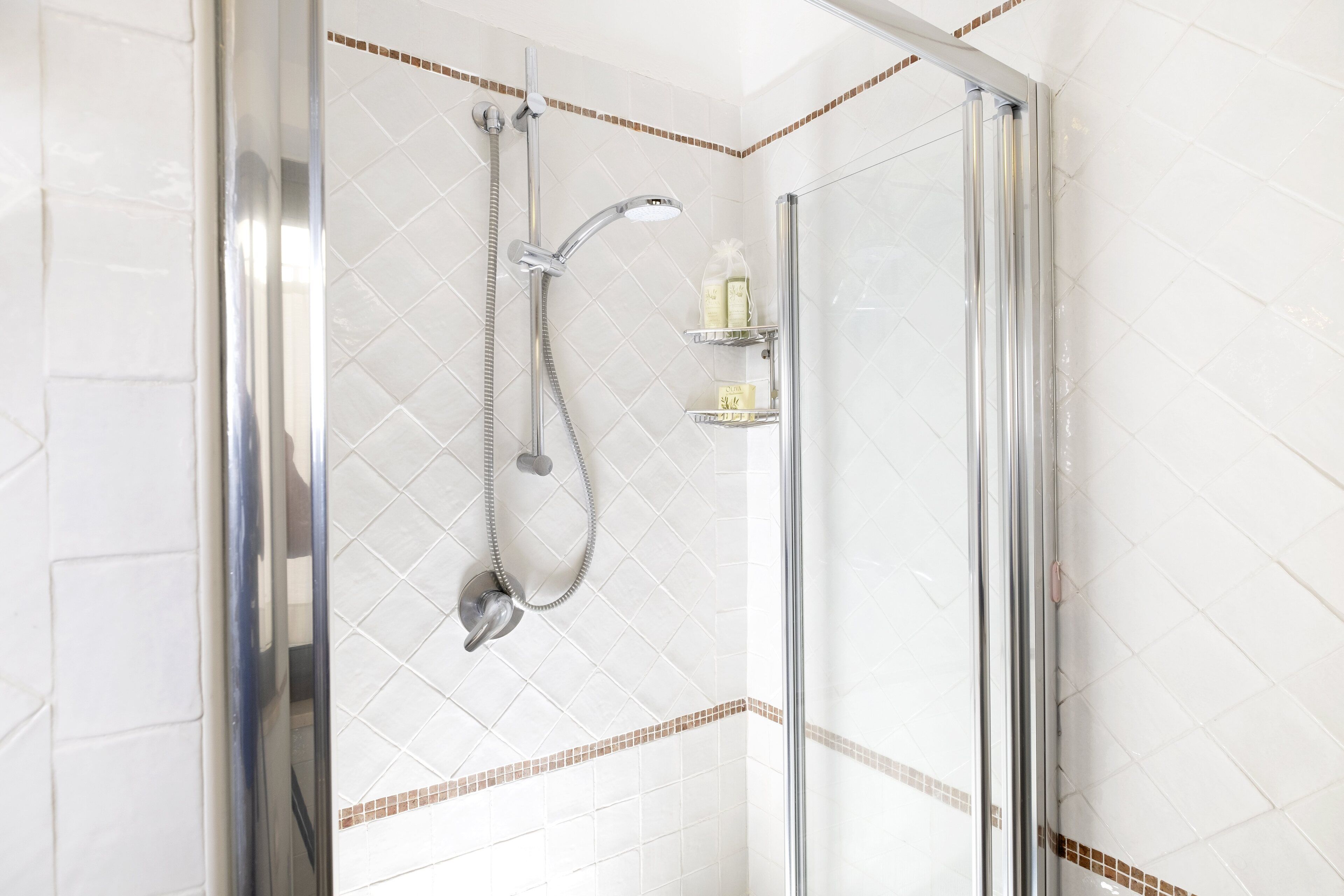 Ducha con cerramiento de vidrio, cabezal de ducha de mano y llave de pared.