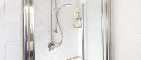 A glass-enclosed shower with a handheld showerhead and a wall-mounted faucet.
