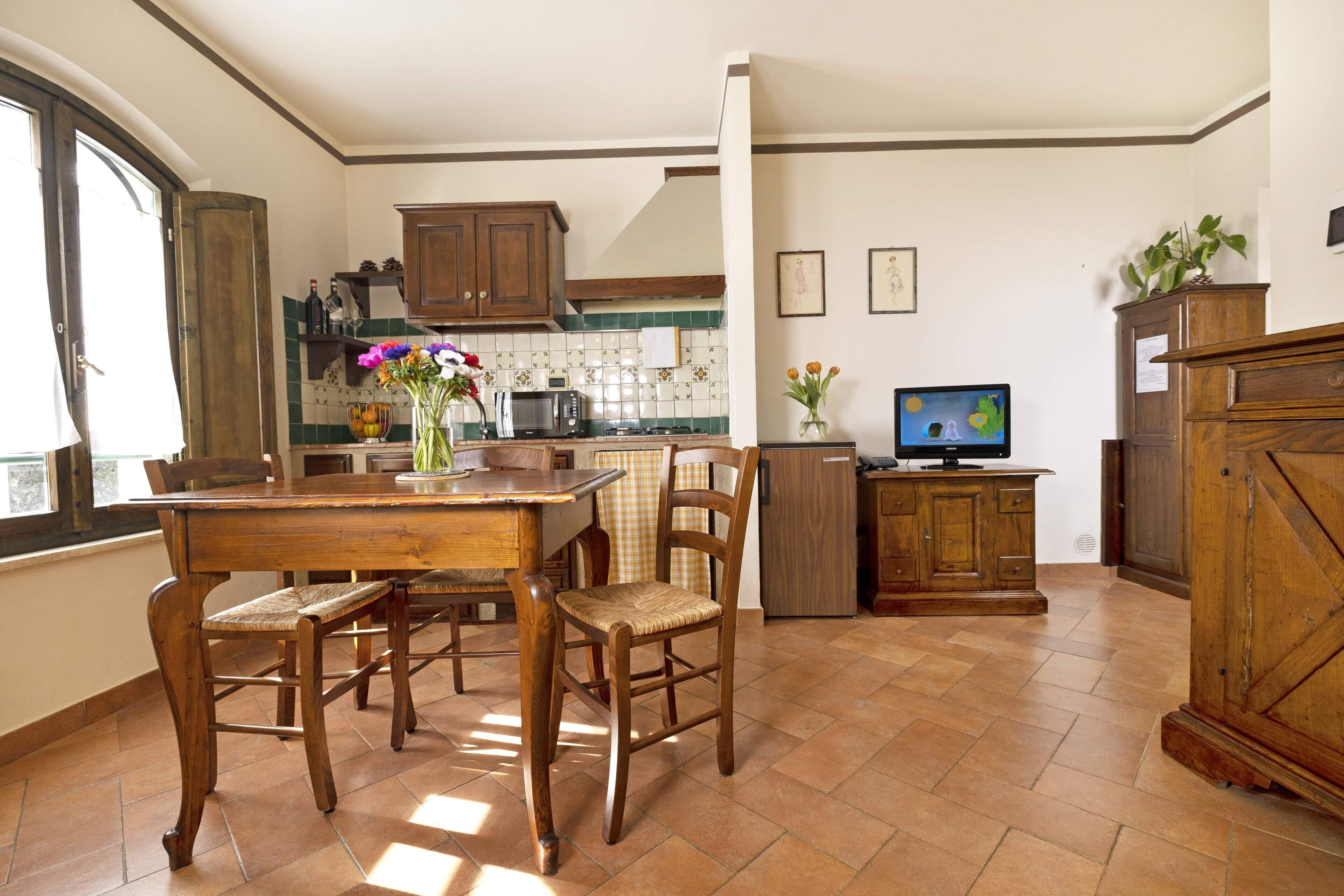 A kitchen with wooden cabinets, a dining table with chairs, a TV, and a window.