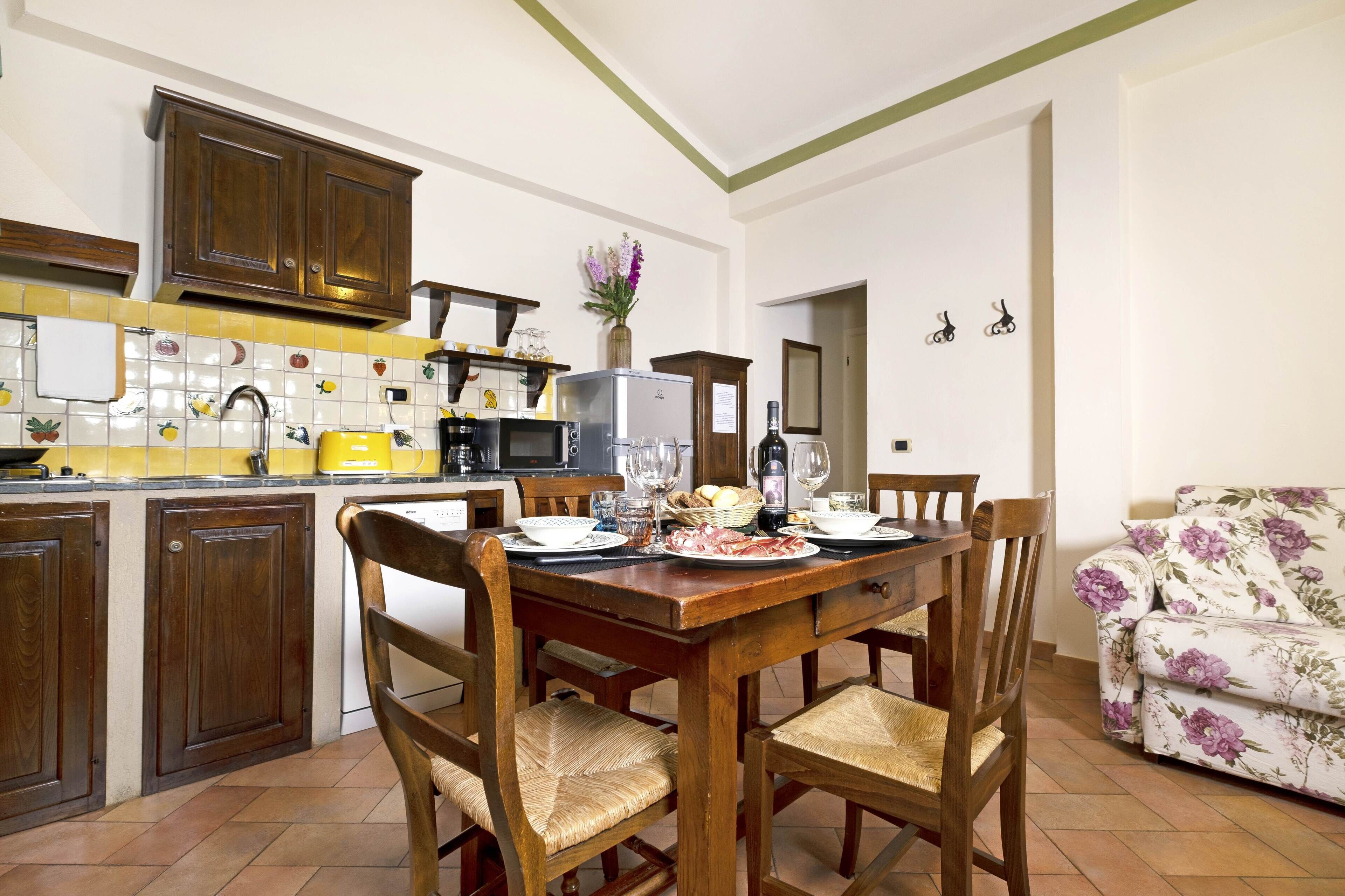 A kitchen with wooden cabinets, a dining table with chairs, and a floral sofa.