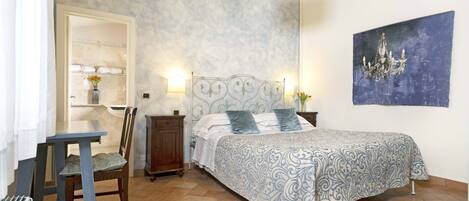 A bedroom with a bed, a desk, a chair, a nightstand, and a wall-mounted light fixture.