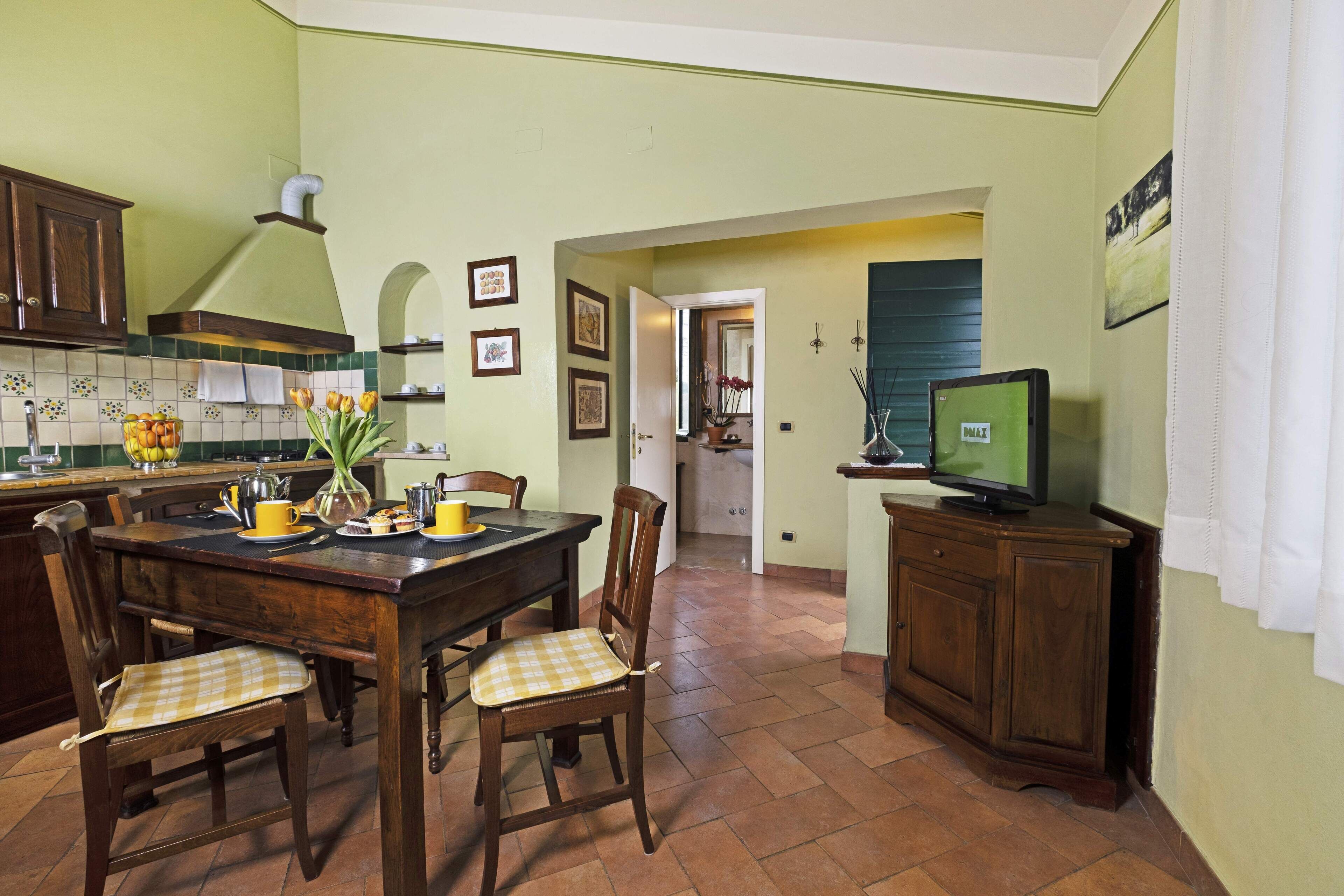 A kitchen with a dining table, chairs, a television, and a cabinet.