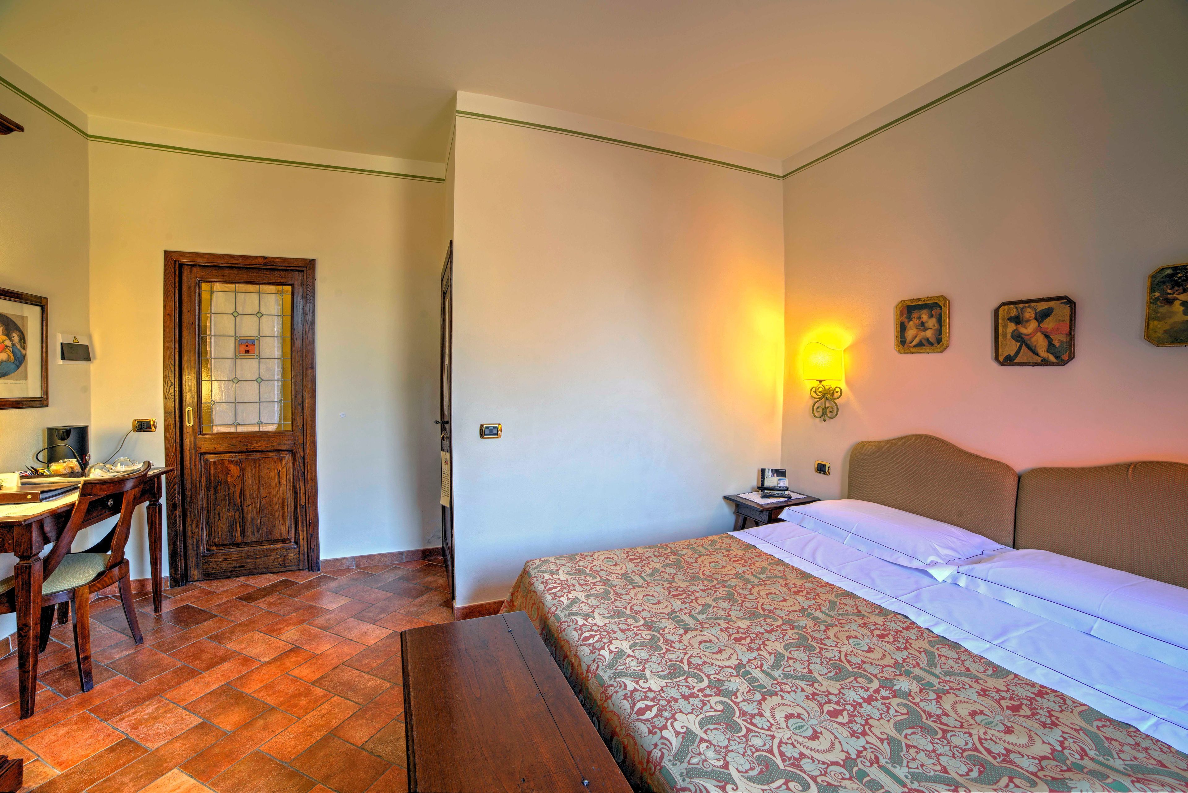 Un dormitorio con cama, un escritorio y una silla, una puerta de madera y una obra de arte en la pared.