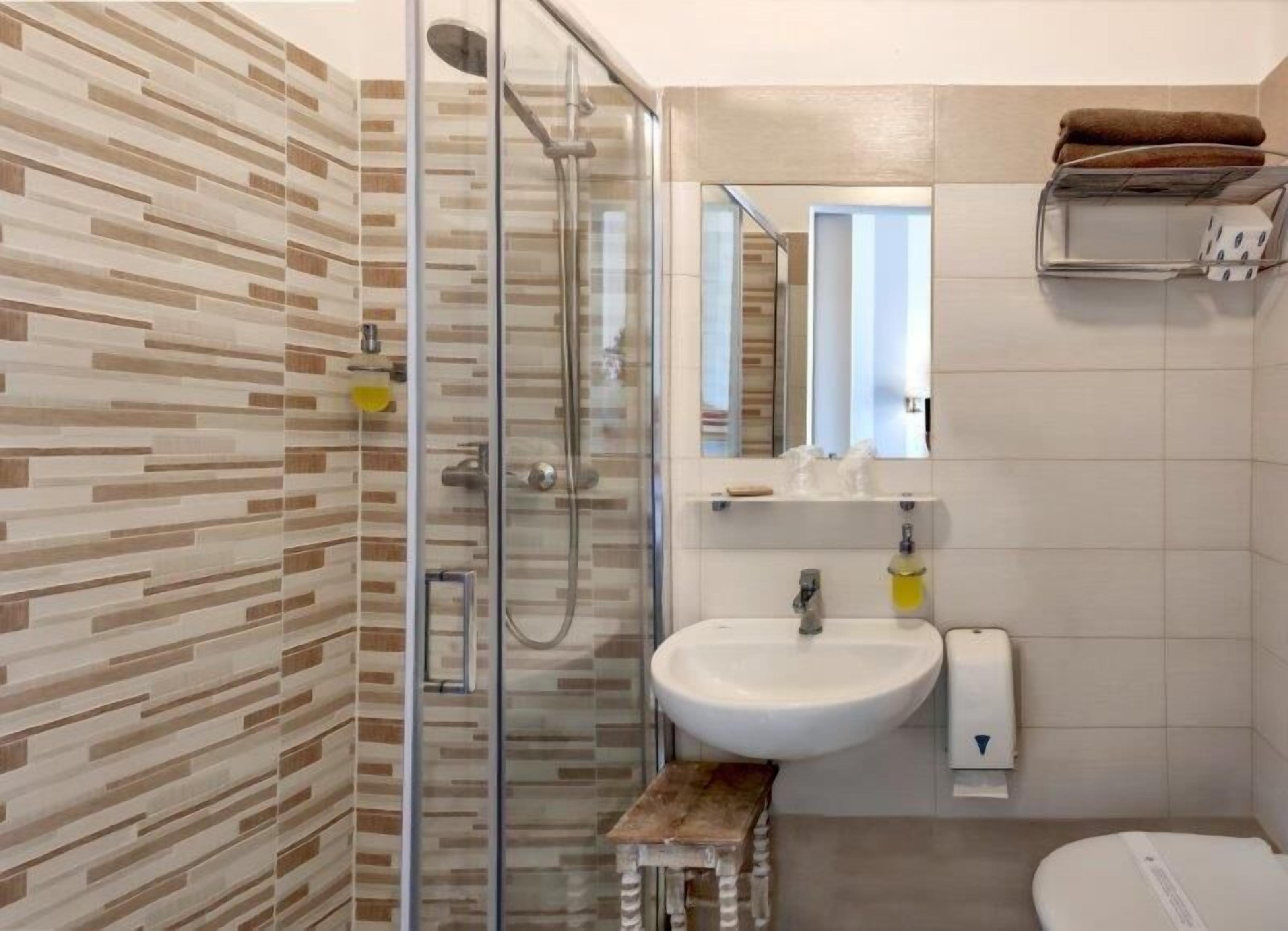Un bagno moderno con cabina doccia in vetro, un lavandino bianco e un piccolo sgabello di legno.