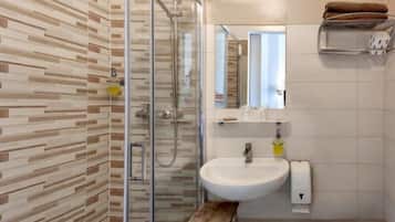 Un bagno moderno con cabina doccia in vetro, un lavandino bianco e un piccolo sgabello di legno.