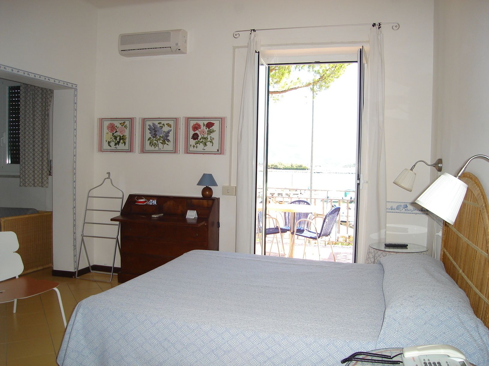 A bedroom with a bed, a desk, a chair, a lamp, and a view of the outside.