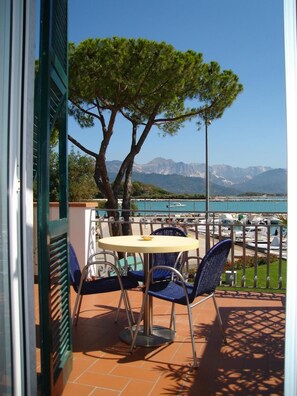 A terrace with a table and chairs, a tree, and a view of a marina and mountains. - Hotel Sette Archi (Ameglia)