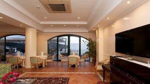 Un salón espacioso con un piano, un televisor de pantalla plana y un balcón con vista al mar.