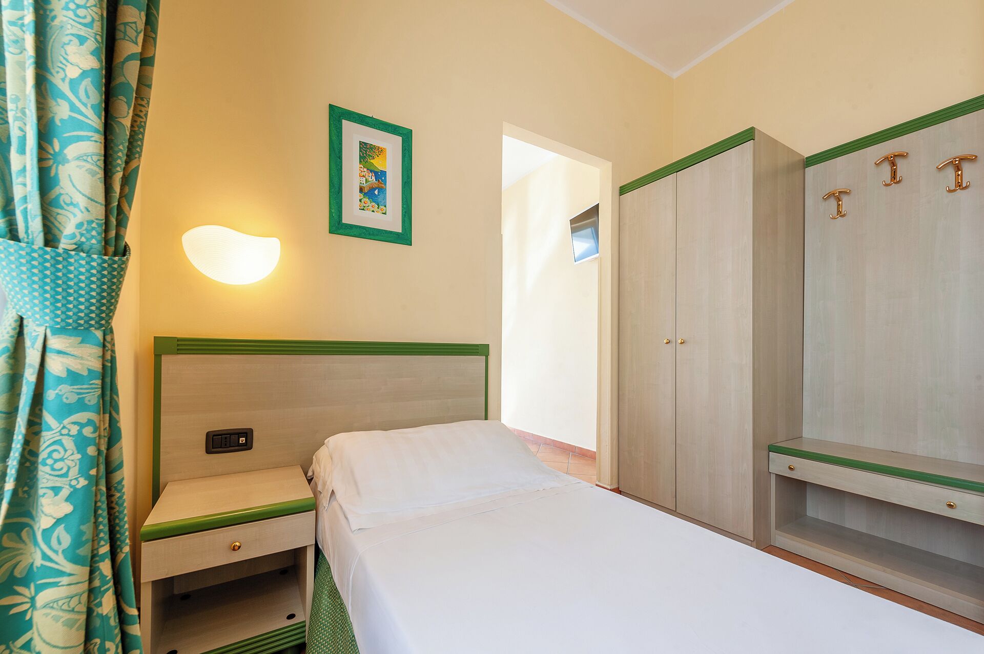 A hotel room with a bed, a nightstand, a wardrobe, and a wall-mounted light.