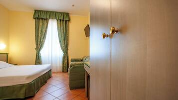 Ein Hotelzimmer mit Bett, Stuhl, Kleiderschrank und einem Fenster mit Vorhängen.