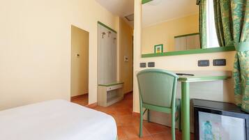 A hotel room with a bed, a desk with a chair, a mirror, and a refrigerator.