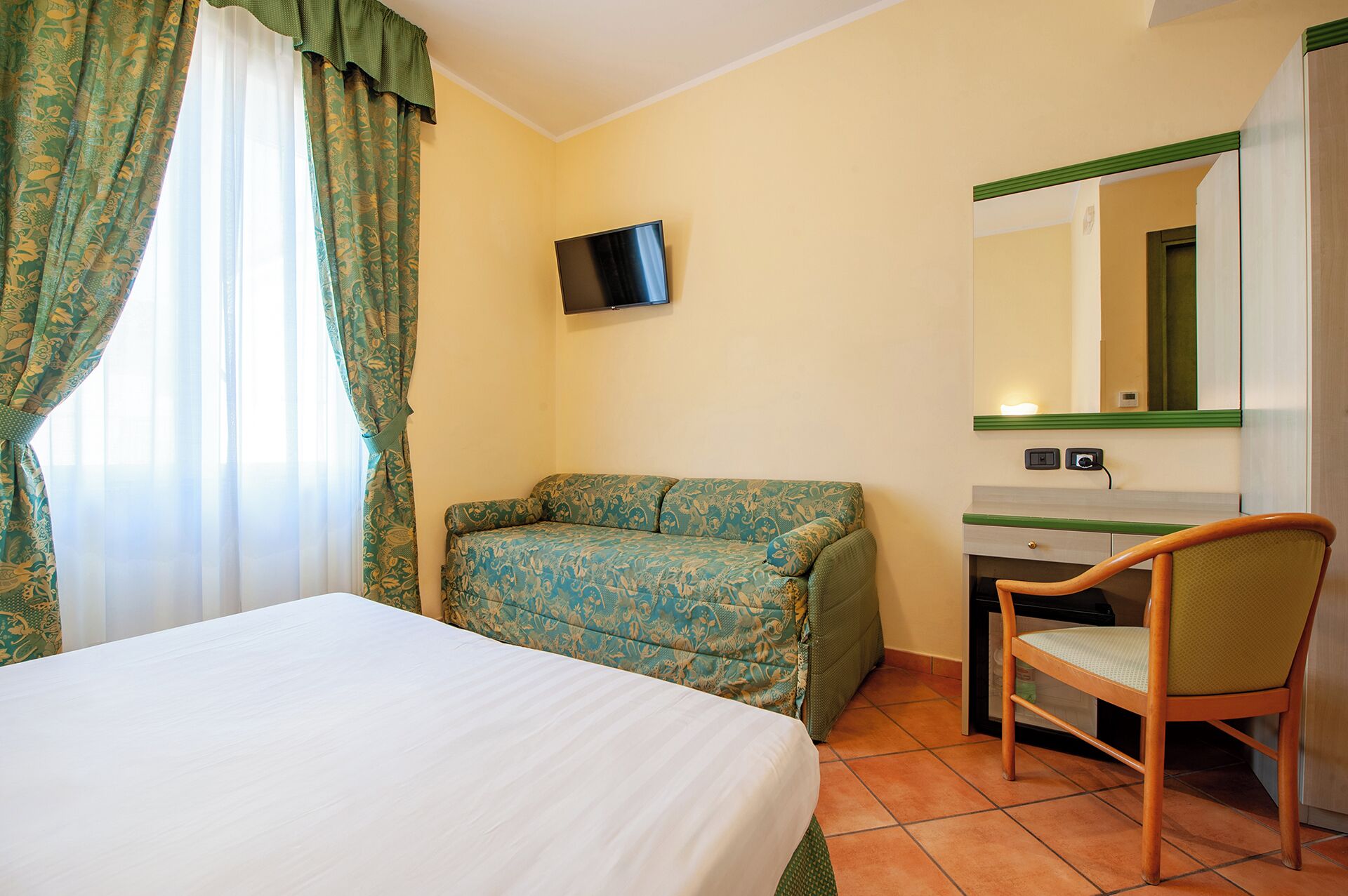 A hotel room with a bed, a desk with a chair, a television, and a mirror.