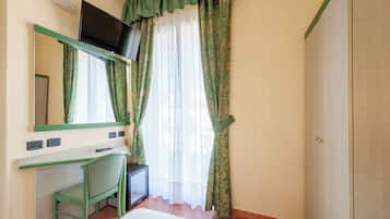 Une pièce comprenant un lit, un bureau avec une chaise, un téléviseur fixé au mur et une porte.