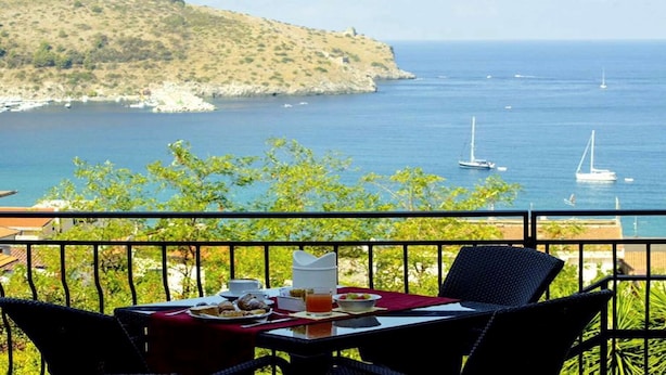 Una mesa con alimentos para el desayuno y vista al mar con barcos.