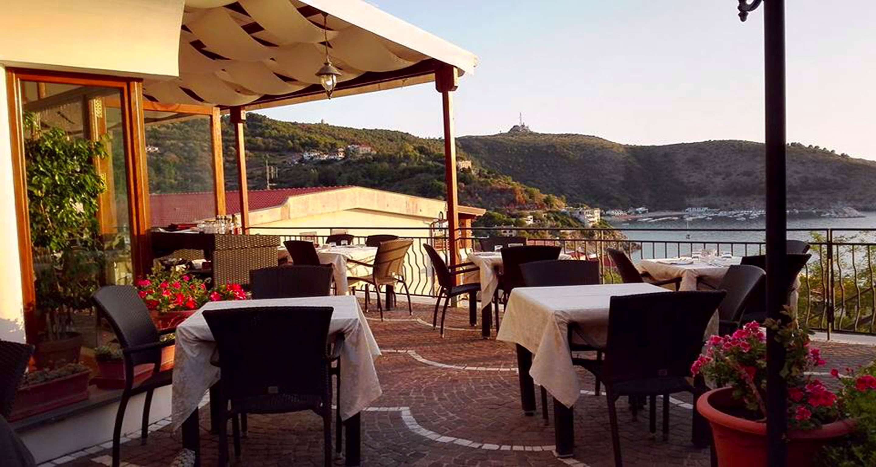 Un espace extérieur aménagé pour les repas, avec des tables et des chaises, offrant une vue sur un paysage côtier.