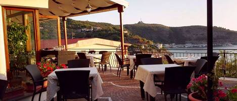 An outdoor dining area with tables and chairs, overlooking a coastal landscape.