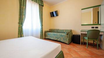 Habitación de hotel con cama, sofá, escritorio, silla, televisor y espejo.