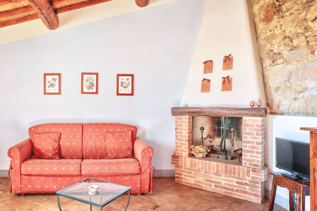 A living room with a red sofa, a glass coffee table, a brick fireplace, and framed pictures on the wall.