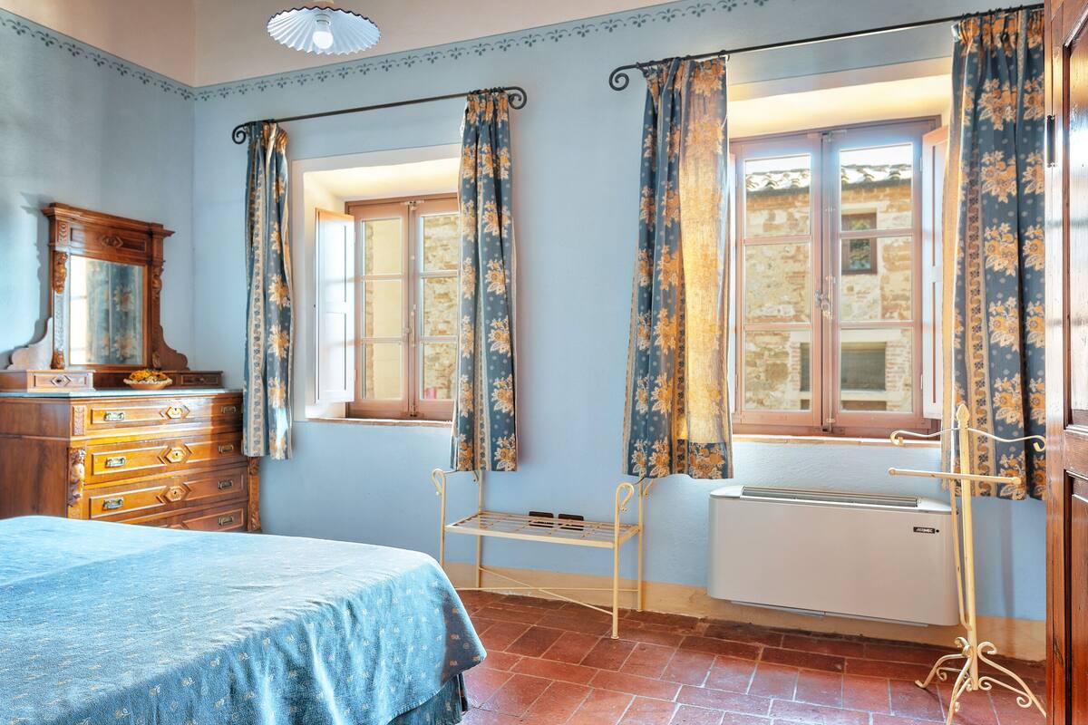 A room with a bed, wooden dresser, radiator, and a window with curtains.