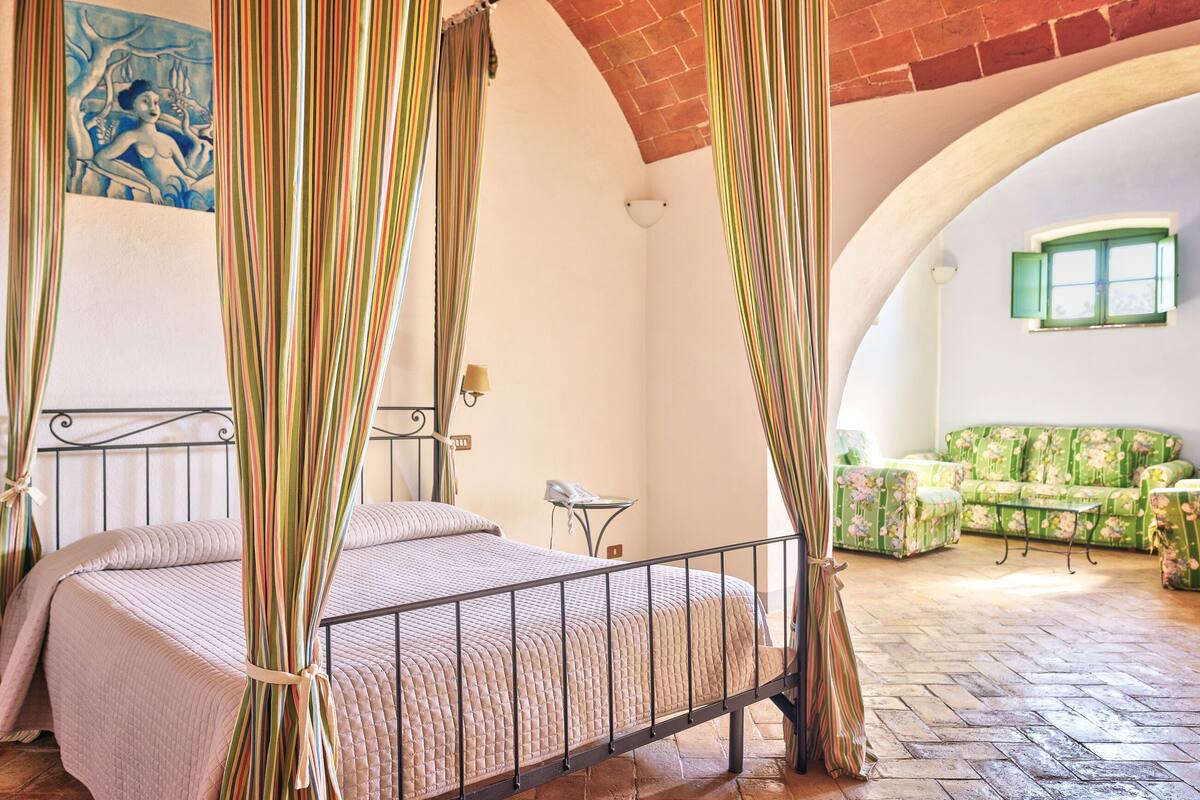 A bedroom with a four-poster bed, a green sofa set, and a mural on the wall.