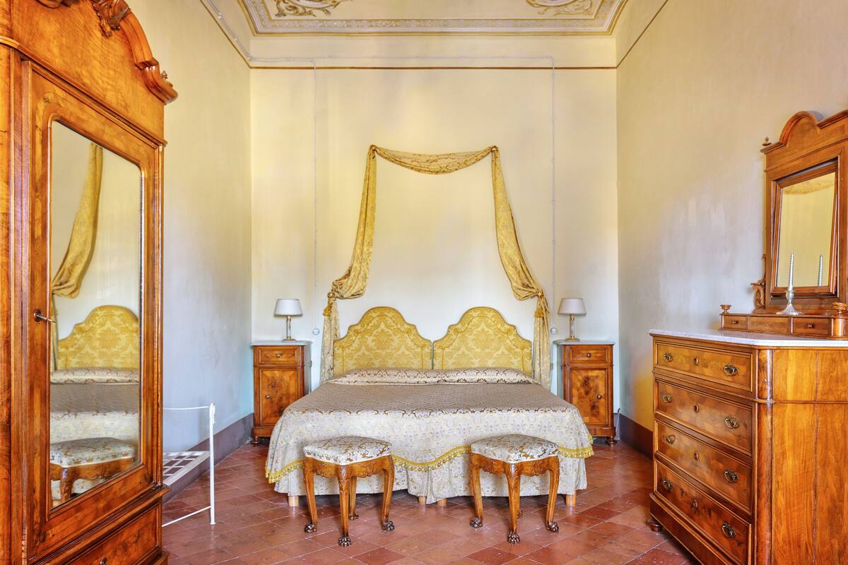 A bedroom with a four-poster bed, two nightstands, a wooden dresser, and a large mirror.