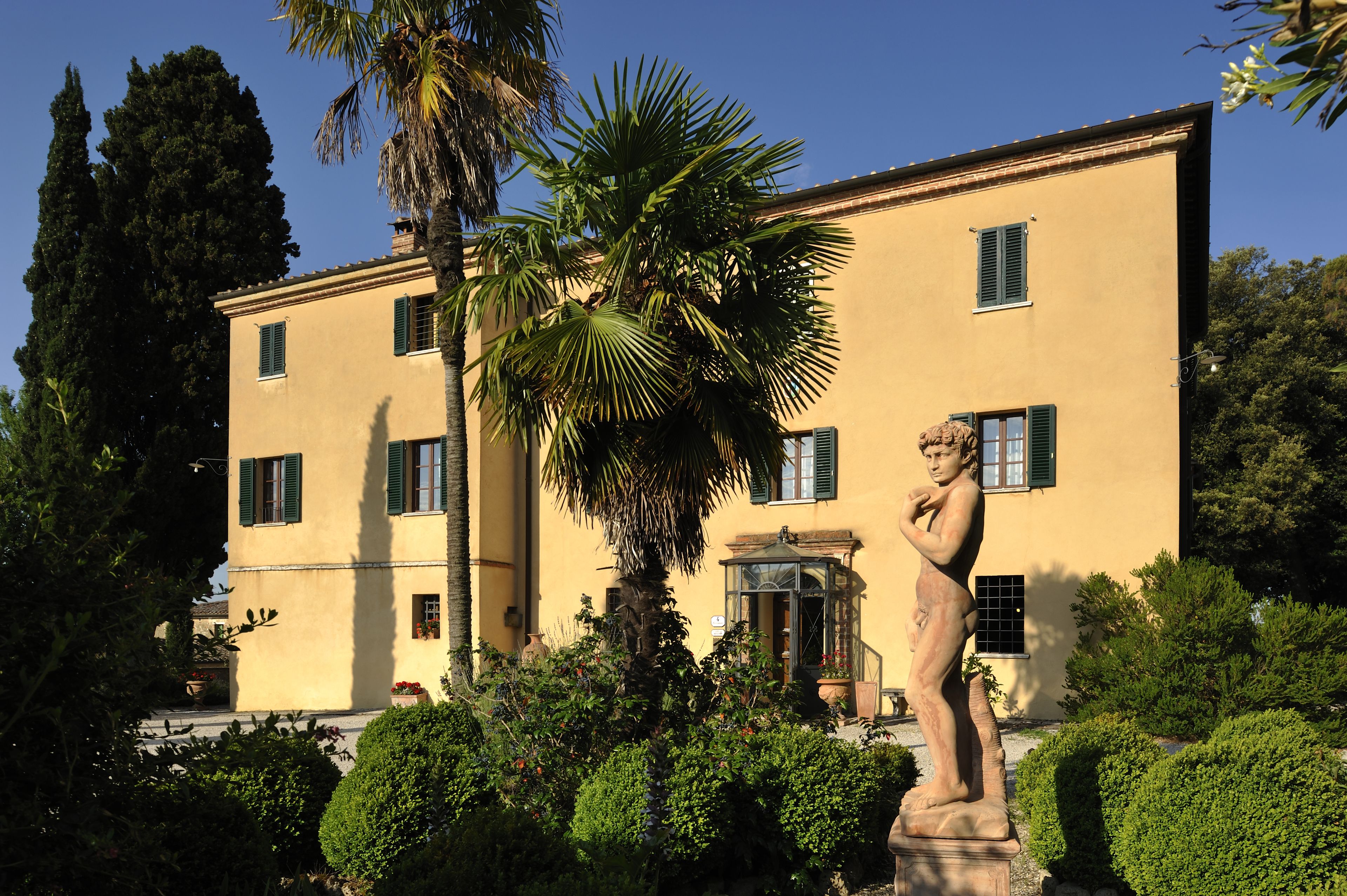 A stately building with a statue in front, surrounded by lush greenery and a tall palm tree.