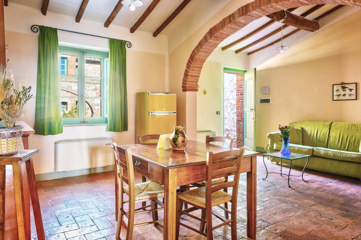 A dining area with a wooden table and chairs, a green curtain, and a brick wall.