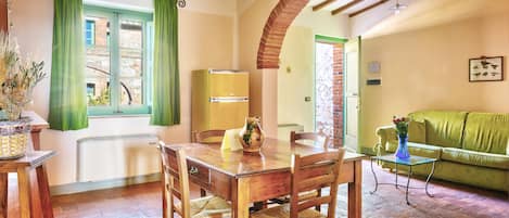 Un comedor con mesa y sillas de madera, una cortina verde y una pared de ladrillo.