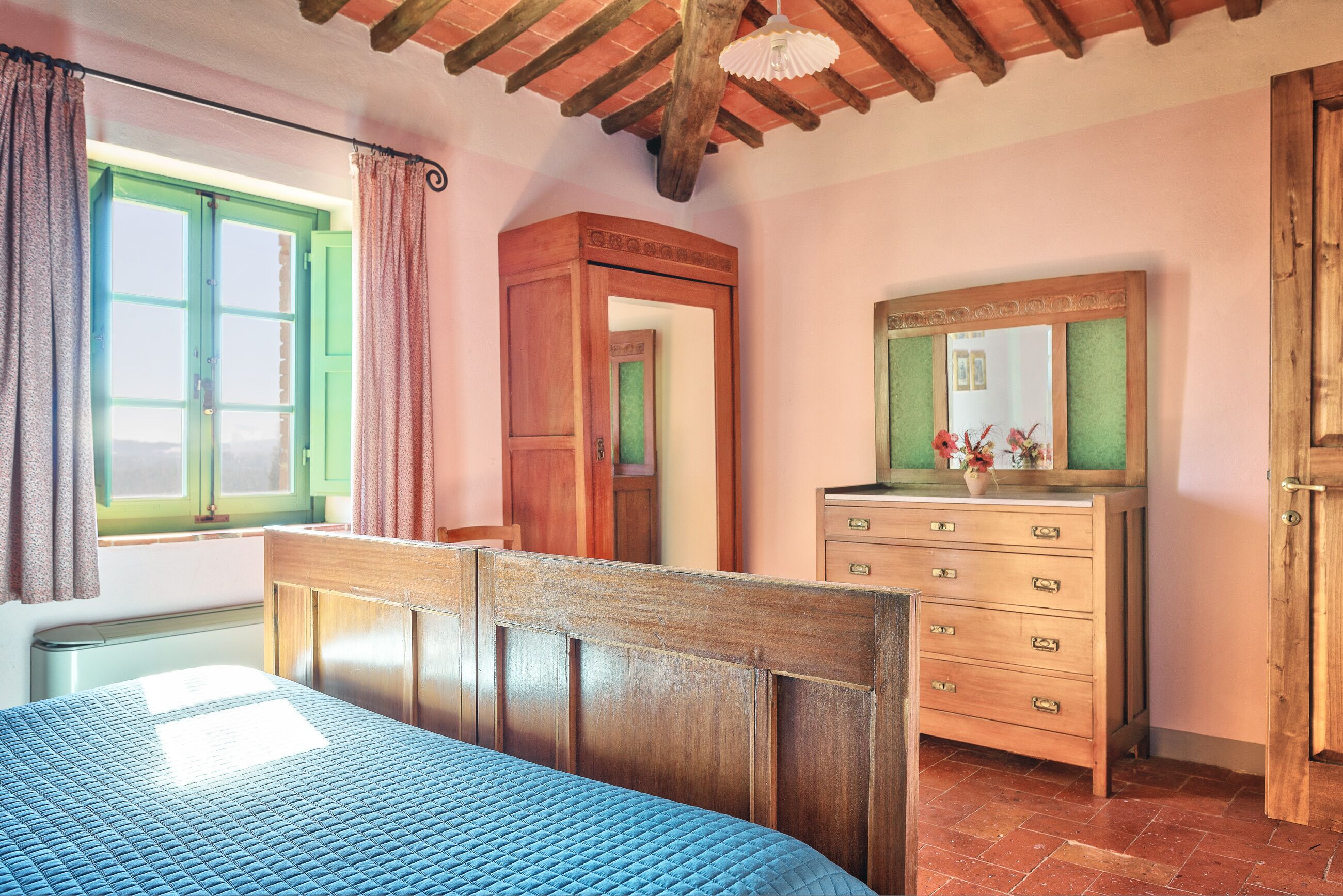 Quarto com cama de madeira, cômoda, espelho e janela com cortinas.