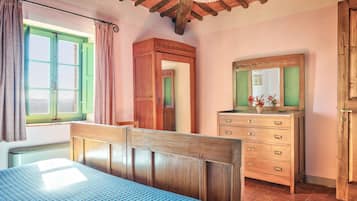 Quarto com cama de madeira, cômoda, espelho e janela com cortinas.