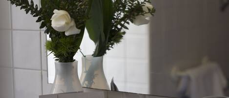 A bathroom with a glass shelf holding a white rose, a small sign, and some stones.