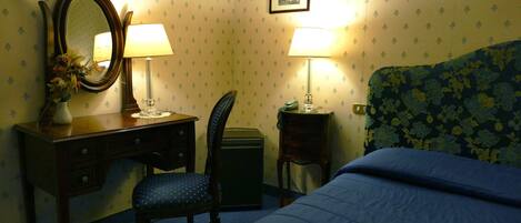 Una habitación de hotel con una cama, un escritorio con espejo, dos lámparas, una silla y una mesita.