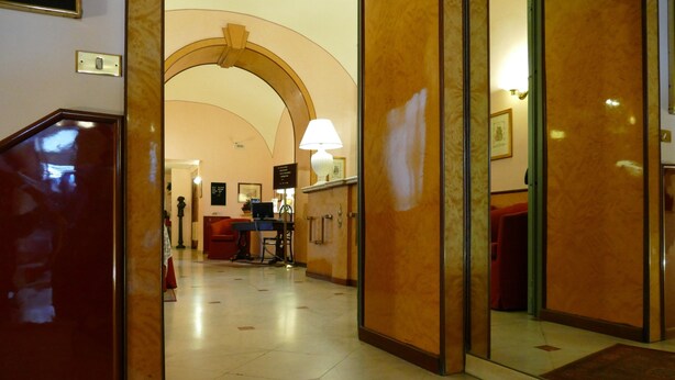 A hotel lobby with a marble floor, a red carpet, and a reception desk with a lamp.