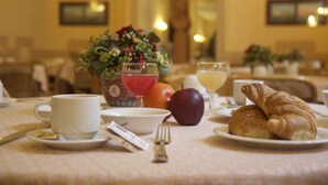 A breakfast setting with a cup, bowl, apple, croissant, and a vase of flowers on a table.