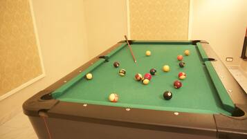 Une table de billard avec des billes, dans une pièce dont les murs sont recouverts d’un papier peint à motifs.