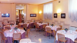 A dining area with round tables, wicker chairs, and white tablecloths.