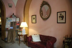 Un hall d’entrée avec un canapé en cuir rouge, une table avec une lampe, un panneau d’affichage avec des cartes et des avis, et un miroir au mur.
