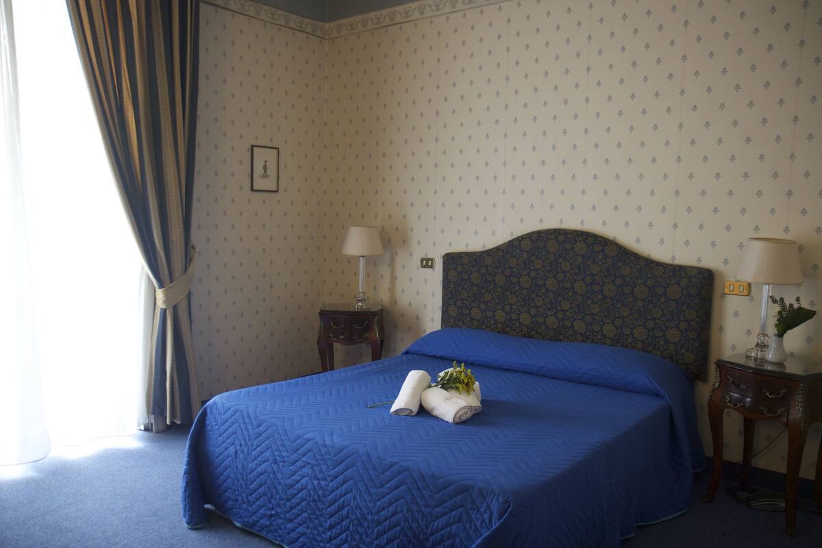 A neatly made bed with blue bedding, a headboard, and a small bedside table with a lamp.