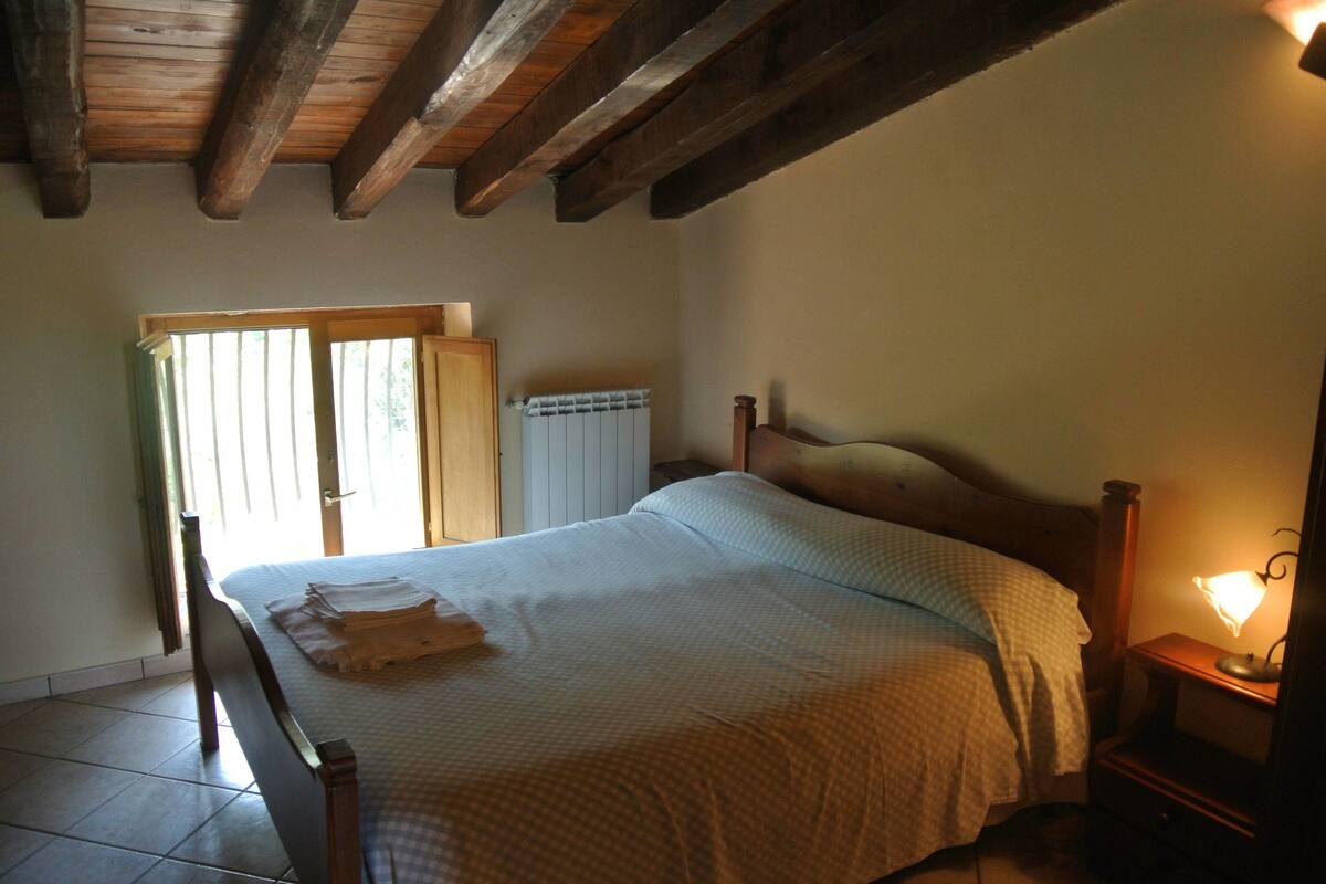 A bedroom with a wooden bed, a nightstand with a lamp, a radiator, and a window with blinds.