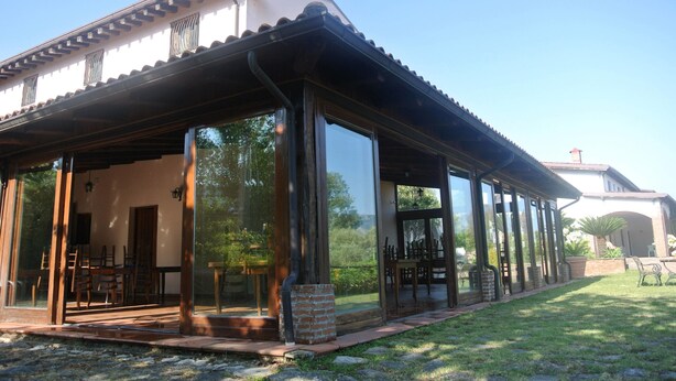 A covered patio with a brick column, wooden furniture, and glass doors leading to an interior space. - Il Forno Antico (San Mauro La Bruca)
