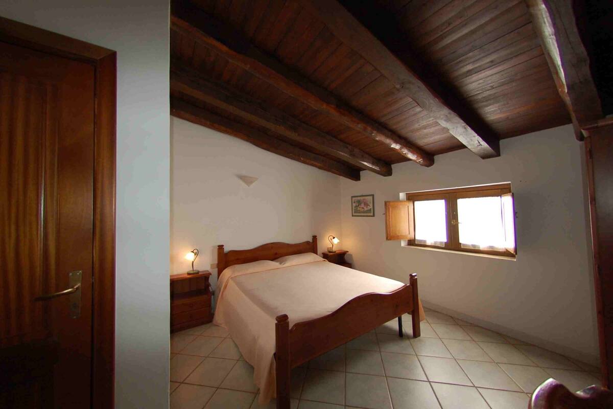 A bedroom with a wooden bed, bedside lamps, a window, and a door.