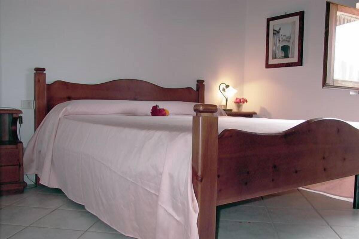 A bedroom with a wooden bed, a bedside table, a lamp, and a framed picture on the wall.