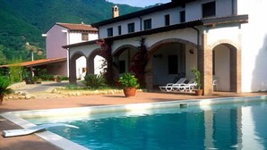 A pool area with a clear view of the pool, lounge chairs, and a building with arches and potted plants. - Il Forno Antico (San Mauro La Bruca)